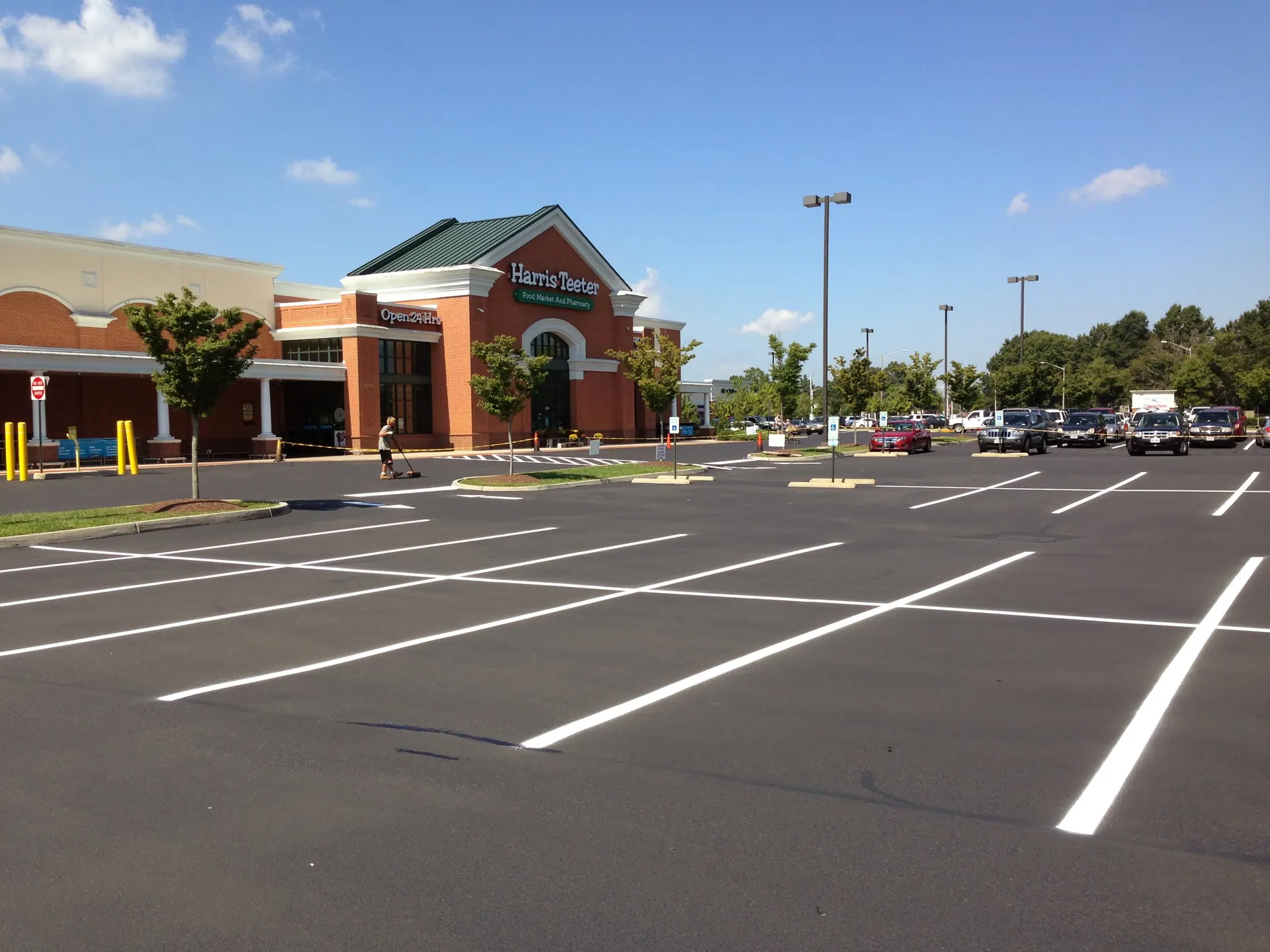 Grocery-anchor lot freshly sealcoated and striped, crew sweeping the entrance
