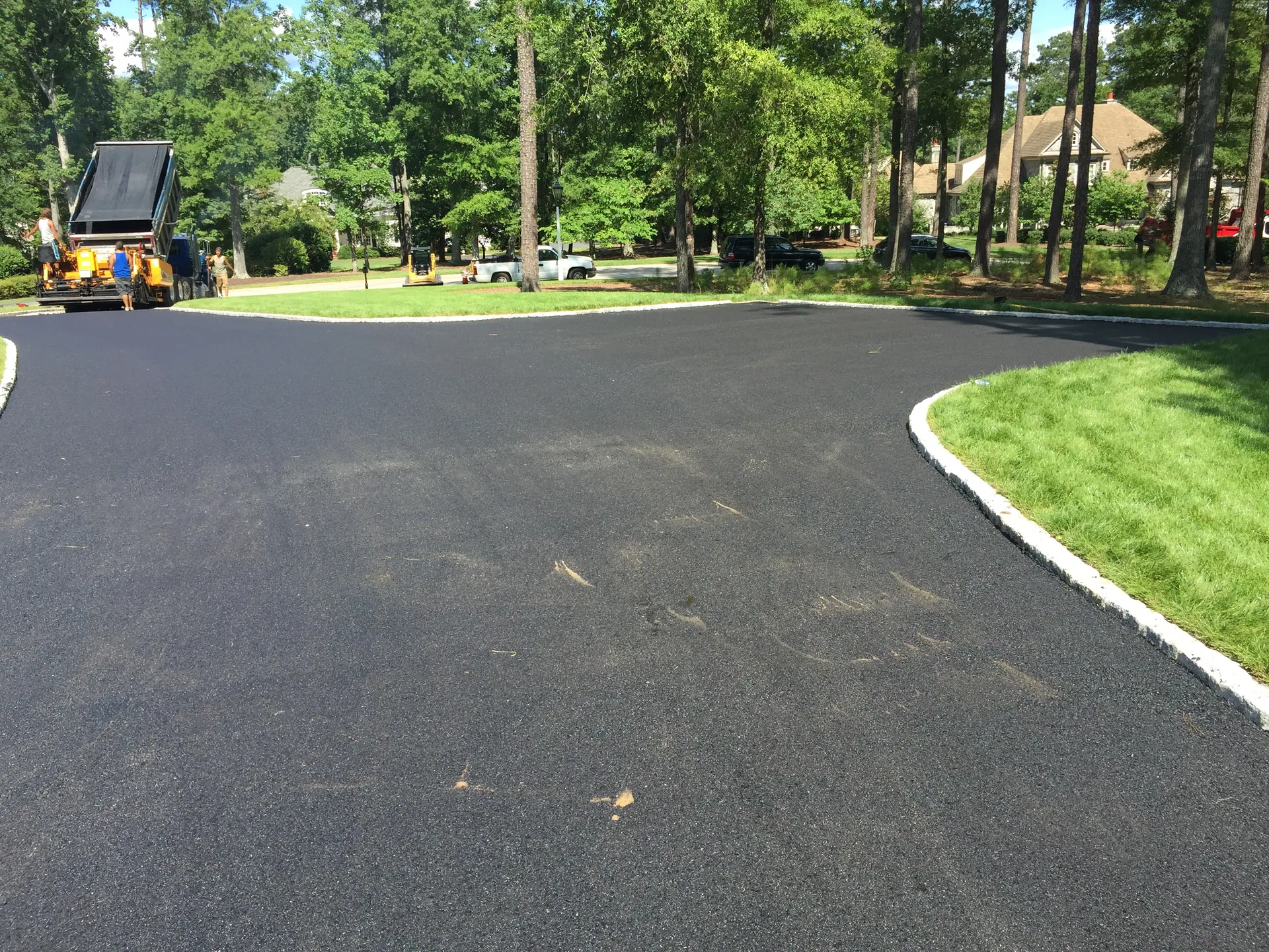 J. Worden and Sons crew laying hot asphalt on a residential driveway with cobblestone borders