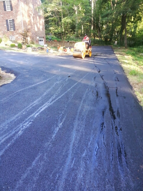 Crew member rolling a long driveway at a brick colonial